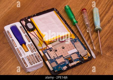 On a wooden table, the tablet is disassembled and screwdrivers for repair Stock Photo