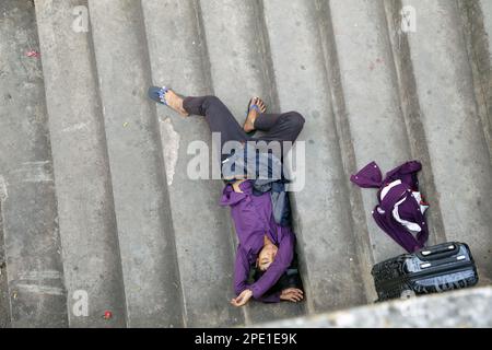 Homeless Asian man in colorful clothes sleeping next to his belongings. Homeless Vietnamese man lying on the stairs Stock Photo