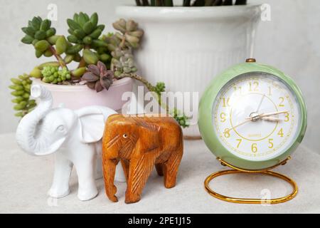 Green vintage style alarm clock showing time in the afternoon. Stylish round clock, elephant figurines and potted succulent plants on a bedside table Stock Photo