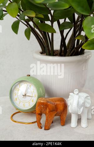 Green vintage style alarm clock showing time in the afternoon. Stylish round clock, elephant figurines and a potted plant on a bedside table Stock Photo