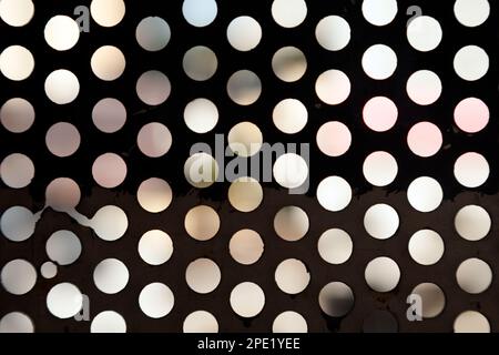 Light coming from outside through round holes in an old black metal sheet. Abstract geometric background with circle pattern Stock Photo