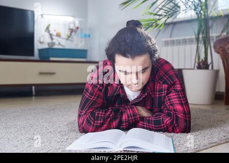 Portrait of young student doing homework while lying on the floor in his room Stock Photo