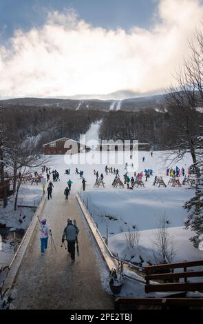 Wildcat Mountain Ski Area, New Hampshire, USA.  Skiers cross creek from the base lodge to the ski area at Wildcat Mountain ski area. Stock Photo