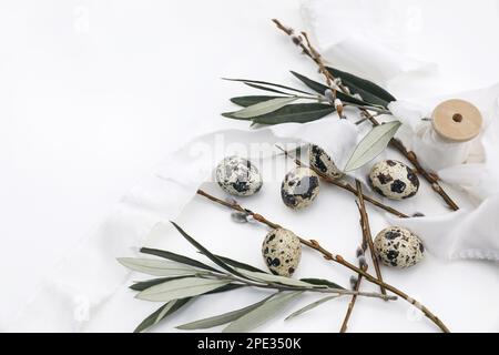 Easter still life. Close-up of mottled Quail eggs, silk ribbons on white table background. Green olive tree branches and catkins. Floral feminine Stock Photo