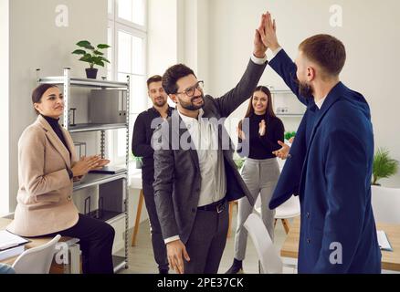 Two male colleagues doing high five at meeting in office Stock Photo