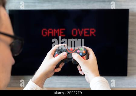 the guy is holding a joystick in his hands against the background of a television screen. gamer and gamepad. The game is over the inscription on the T Stock Photo