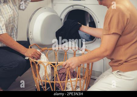 Senior couple working together to complete their household chores at the washing machine in a happy and contented manner. Husband and wife doing the Stock Photo