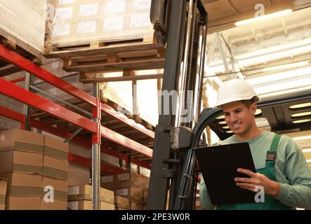 Worker near forklift truck with cardboard boxes in warehouse. Logistics ...