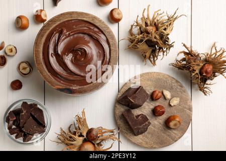 Bowl of tasty chocolate paste with hazelnuts on white wooden table, flat lay Stock Photo