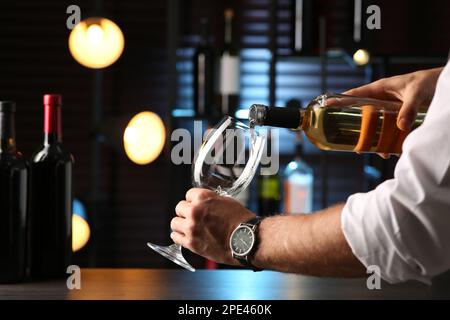 Man pouring white wine into glass indoors, closeup Stock Photo