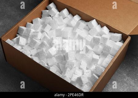 Cardboard box filled with polystyrene styrofoam pieces on grey table, closeup Stock Photo