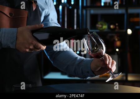 Bartender pouring red wine from bottle into glass indoors, closeup Stock Photo