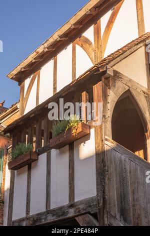 A historic half-timbered whitewashed building. A stairway runs up to an arched doorway leading onto a gallery with window boxes. A clear blue sky is a Stock Photo