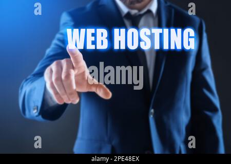 Businessman pointing at phrase WEB HOSTING on virtual screen against dark background, focus on hand Stock Photo