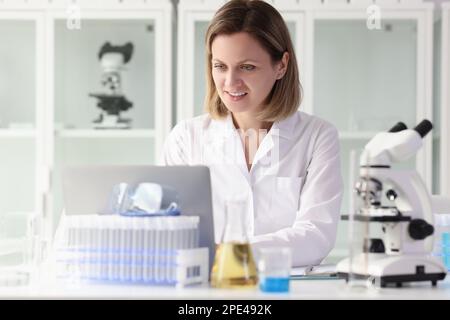 Satisfied female researcher working on laptop at laboratory table. Stock Photo