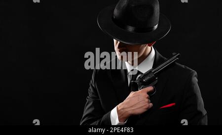 Gangster from 1940s with a gun. Man in a black suit and hat with a gun over dark background. Photo with a copy space. Stock Photo
