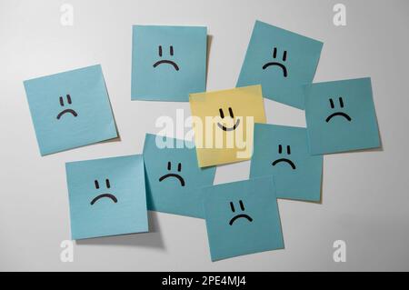 Sticker notes on the white background. Sticky note papers with smiley. One is different. One happy smiling face among sad ones. Stock Photo