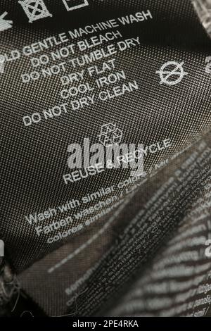 Fabric composition label, Washing instructions and recycling sign on black fabric label. Laundry tag on clothes. Stock Photo