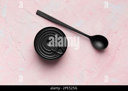 Black matte round closed tin can and black spoon on texture background top view, tinned food, canned food, preserves. Stock Photo