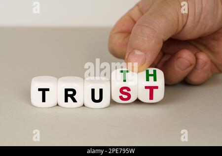 On a gray surface are white cubes with the inscription - TRUTH or TRUST. Two dice in hand. Business concept. Stock Photo
