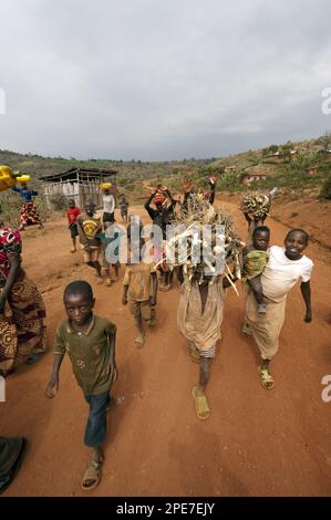 Boys carrying firewood on heads walk along the dusty village road, Rwanda Stock Photo