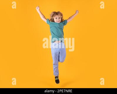 Energetic kid boy jumping and raising hands up on isolated studio background. Full length body size photo of jumping high child boy, hurrying up runni