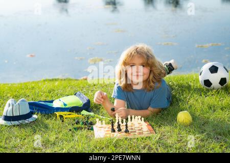 Chess school outdoor. Child laying on grass in spring park and think about chess game. Child education concept. Intelligent, smart and clever school k Stock Photo