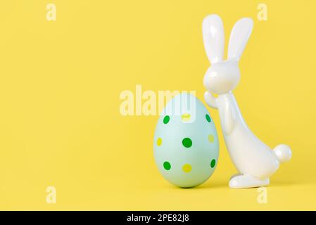 Happy Easter. Close-up of easter egg next to easter bunny with copy space for text against yellow background Stock Photo