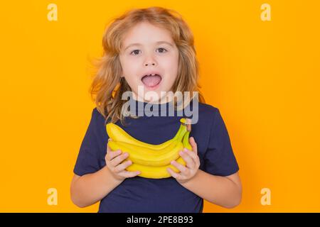 Vitamin and healthy fruits for kids. Child hold banana in studio. Studio portrait of cute kid boy with bananas isolated on yellow background, copy Stock Photo