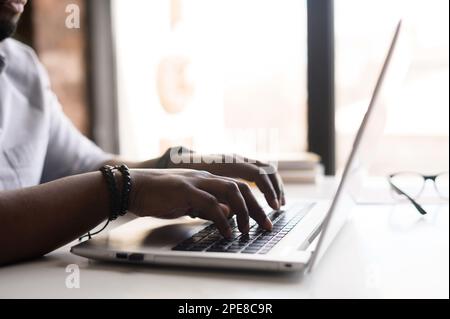Male hands on the keyboard of laptop. Male african-american office employee in casual shirt working with laptop computer, face is not visible Stock Photo