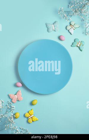 Easter banner on a blue background. Empty blue plate for text, Easter eggs and cookies in the shape of a rabbit and a butterfly. Easter concept. Stock Photo