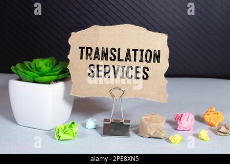 On a light background, gold-framed glasses, a flower in a pot, a green notebook, a red pen and a brown notebook with the text TRANSLATION SERVICES. Bu Stock Photo