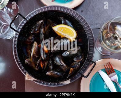 Steamed mussels in shells with lemon in metal serving pan Stock Photo