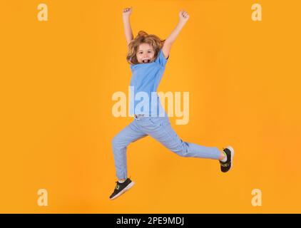 Full length of excited kid jumping. Energetic kid boy jumping and raising hands up on isolated studio background. Full length body size photo of Stock Photo