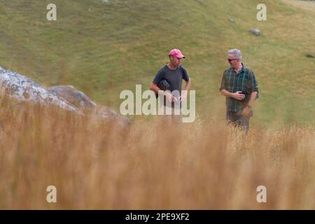 Two people talking to each other in a distance, on a day walk amongst hills, Castle Hill, New Zealand. Stock Photo