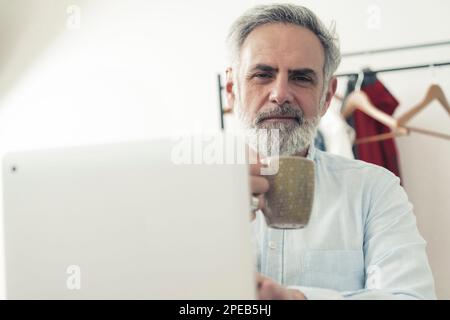 Gray haired bearded male entrepreneur holding a cup of coffee and looking at the camera. High quality photo Stock Photo