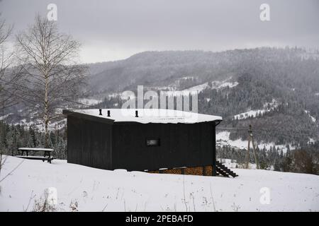 Black wooden tiny cabin with view on snowy pine forests in Ukraine Stock Photo