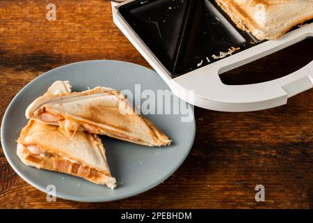 Freshly made toasted sandwiches from a sandwich maker on a plate on a wooden rustic background. Toasted triangular sandwiches with cheese. Stock Photo