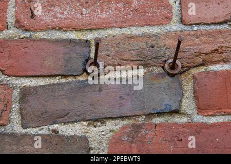 Two (2) rusted nails on old brick wall of red color.  Textured background of masonry on vintage building. Bricks are laid uneven. Stock Photo