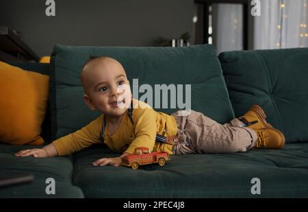 Cute baby boy in yellow shirt lying on green couch Stock Photo