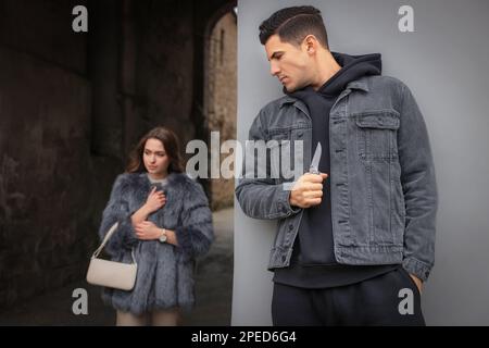 Criminal with knife hiding behind wall and waiting for victim near alley Stock Photo