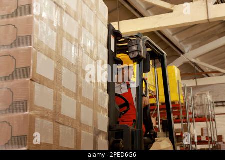 Worker sorting cardboard boxes with forklift truck in warehouse ...
