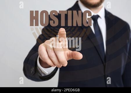 Businessman pointing at word HOSTING on virtual screen against light background, focus on hand Stock Photo