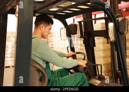 Worker sorting cardboard boxes with forklift truck in warehouse. Logistics concept Stock Photo