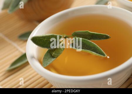 Cup of aromatic sage tea with fresh leaves on table, closeup Stock Photo