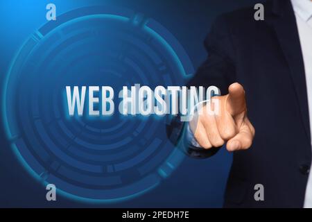 Businessman pointing at phrase WEB HOSTING on virtual screen against blue background, closeup Stock Photo