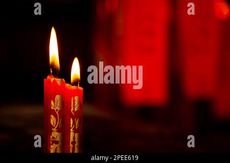 2 red candles, decorated with gold floral pattern, in a Chinese Taoist temple. Two wax candles burning in a dark room Stock Photo