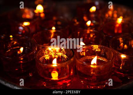 Close-up photo of a lot of red candles in glasses burning in a Chinese Taoist shrine at night. The flickering flames of the candles create a sacred at Stock Photo