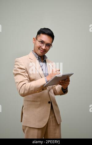 Portrait of handsome and successful millennial Asian businessman in formal business suit and glasses using his tablet and looking at the camera while Stock Photo