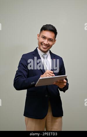 Portrait, Smiling and happy millennial Asian businessmen in formal business suit using his digital tablet and looking at the camera while standing aga Stock Photo